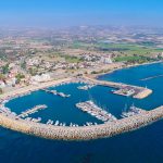 Aerial bird's eye view of Zygi fishing village port, Larnaca, Cyprus. The fish boats moored in the harbour with docked yachts and skyline of the town near Limassol from above.